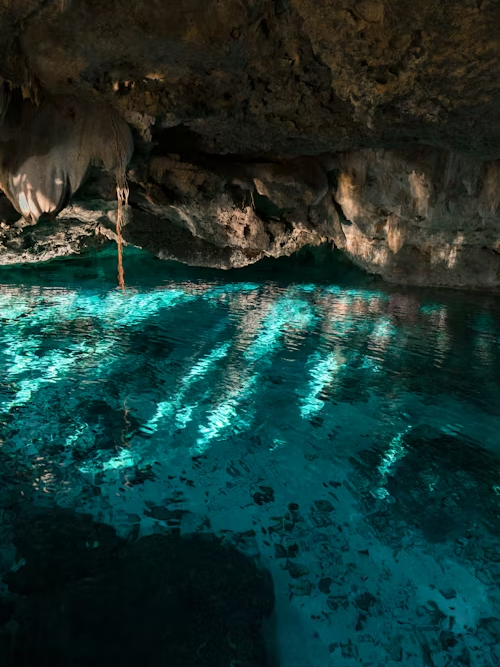 Clear blue water inside a shaded cenote with rock formations in Mexico