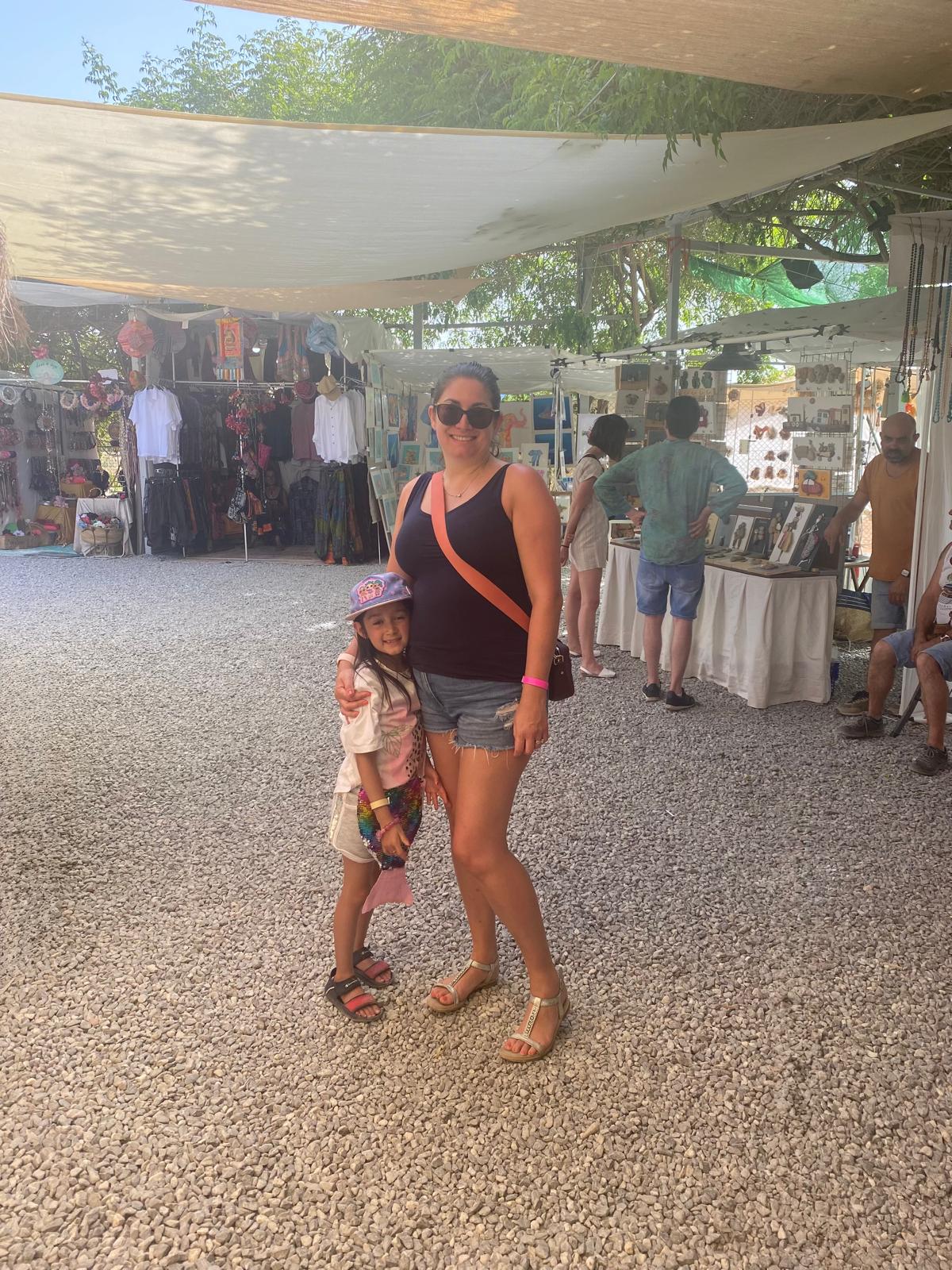 Adult and child standing together at a shaded outdoor hippie market in Ibiza