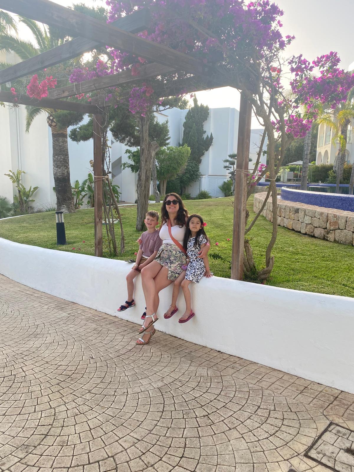 Adult sitting with two children on a low wall in a sunny resort garden setting