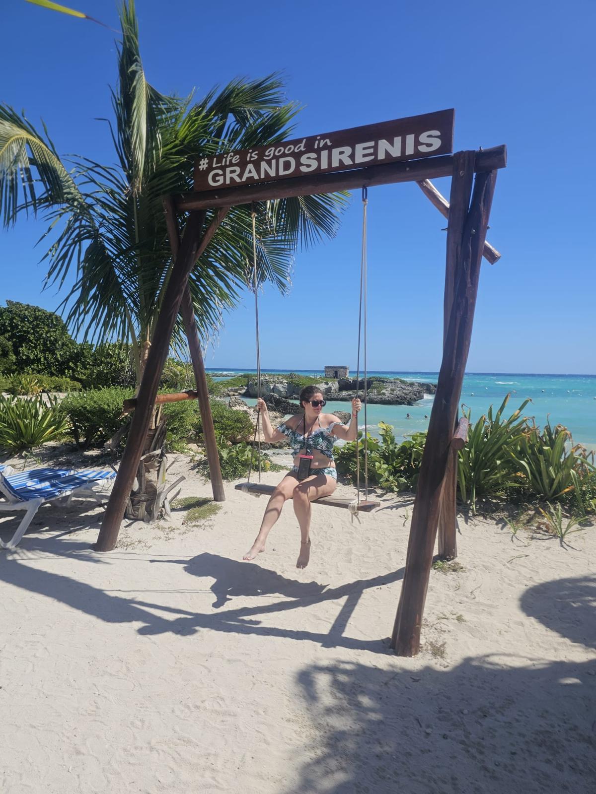Person sitting on a wooden swing on a sandy beach with sea and palm trees in Mexico